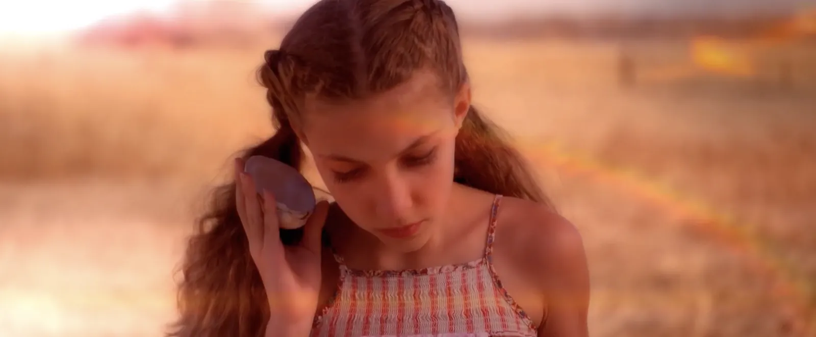 Girl holding a shell to her ear in a sunlit field