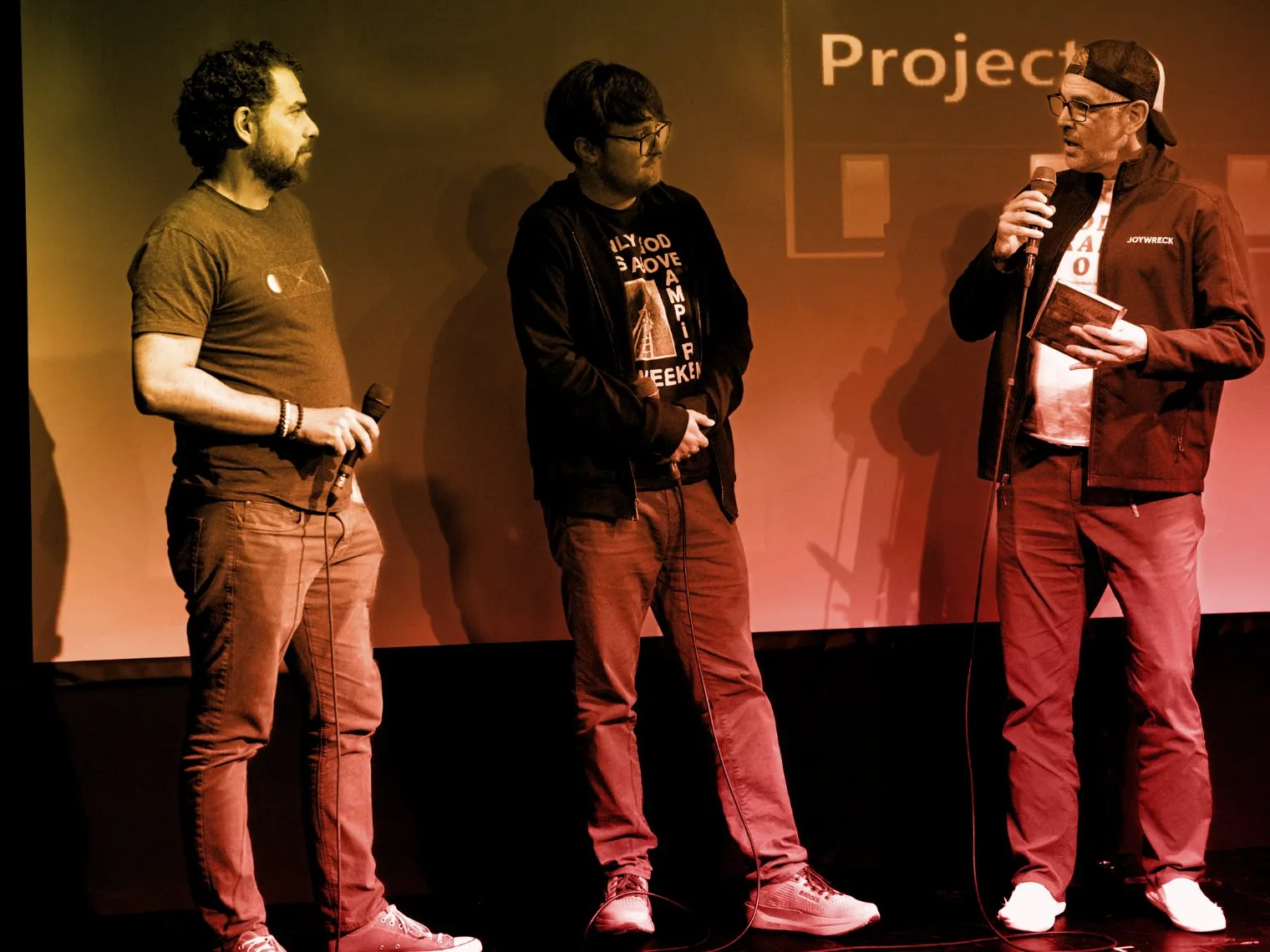 Three filmmakers with microphones on stage in front of a projected Emerging Filmmaker Project title card