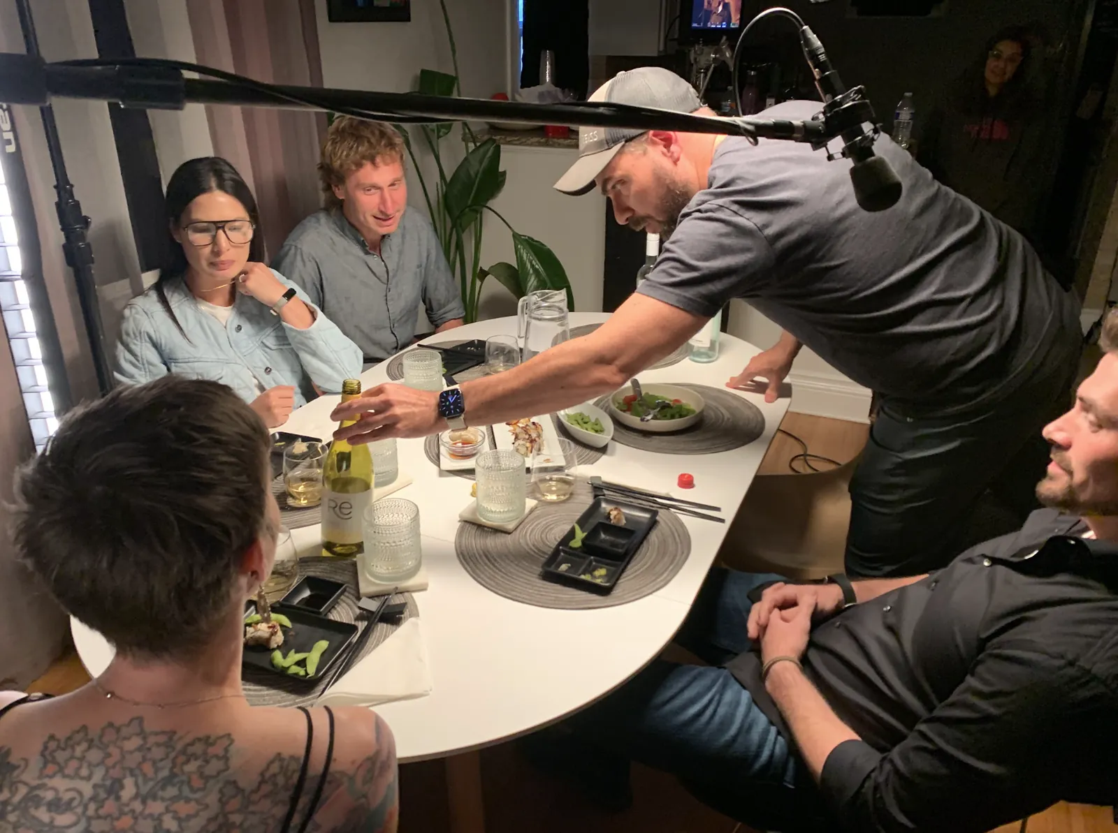Director adjusting a wine bottle on the dinner table with cast seated around it